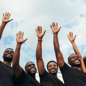 Cheerful black men and woman raising hands against a blue sky